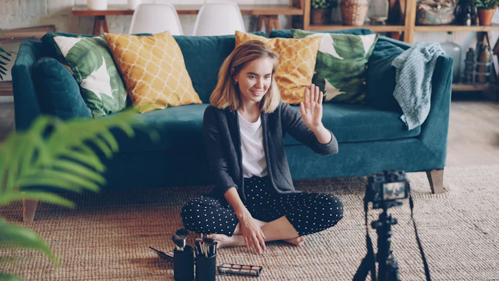 A young woman waving at the camera while filming a makeup tutorial