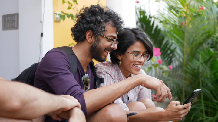 A man and a woman laughing while looking at a smartphone together