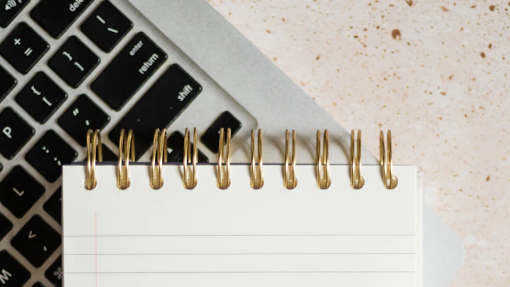 A notepad, pen and laptop laid out on a white desk