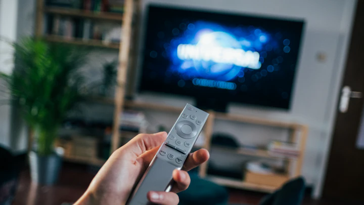A hand holding a remote control in front of a television